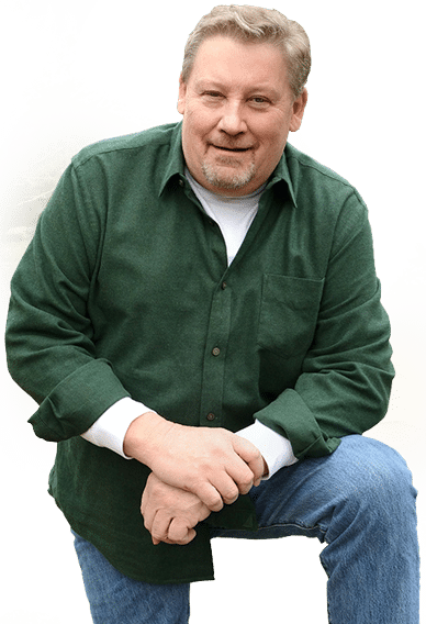 Steve Ding kneeling outdoors, wearing a dark green button-up shirt and jeans, smiling at the camera.